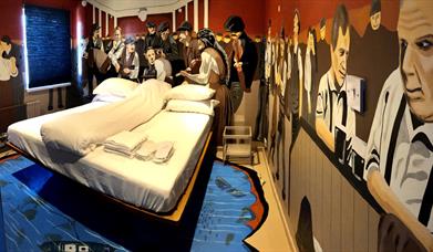 A photo of a Titanic-themed bedroom with murals of passengers on the ship, surrounding a double bed.