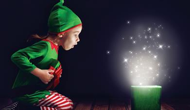 Child dressed as an elf opening a magical present.