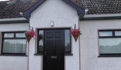 Image of the front of a white bungalow with flower baskets hanging on either side of the door