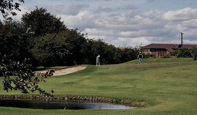 Men playing golf on a course with a pond and a sand bunker.