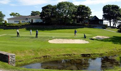 Image is of golf course with golfers playing and lake in the foreground