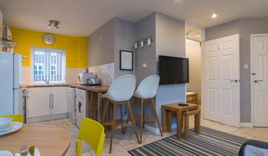 A photo of a kitchen which wraps around a wall with a tv to a living space.