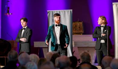 3 individuals in suits performing opera in a church venue