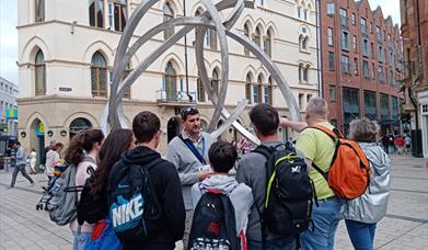 A tour group listening to a guide at a sculpture in Belfast city centre.