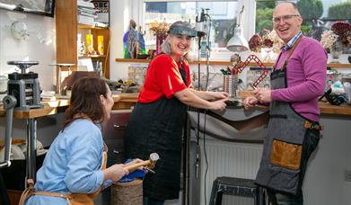 Man and Two Ladies Creating Jewellery in a Goldsmiths Workshop, Everyone is Smiling