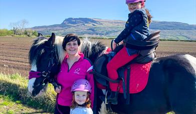 a woman and two children pose with a horse with Binevenagh Mountain in the background