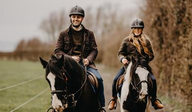 a man and woman on horseback on a countryside trail