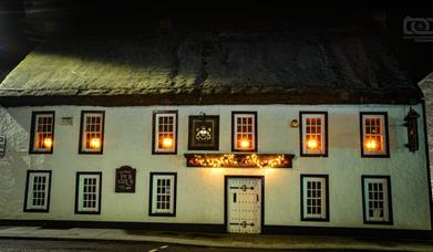 Night time exterior of the Thatch Inn Bar & Restaurant - white building with thatched roof and lights on in the upper windows