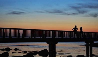 Couple standing on wooden pier looking at the sunset  at Ballycastle Beach.
