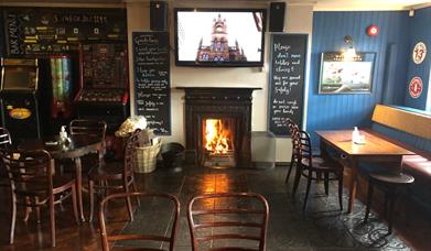 Image is of the lounge area of the bar with open fire blazing and table and chairs