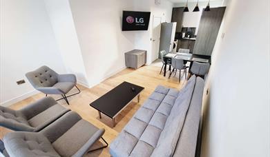 Living room with a suite, coffee table and tv leading to a kitchen with dining area and fridge.