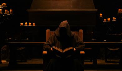 Hooded figure storyteller sitting in Winterfell Hall