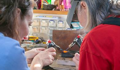 Two ladies with small torches melting down some gold in contemporary studio