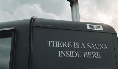 Side of matte black sauna with writing reading "there is a sauna inside here"