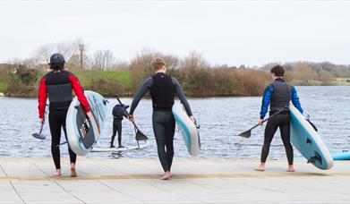 image of 3 males heading towards the lake carrying SUP paddle boards