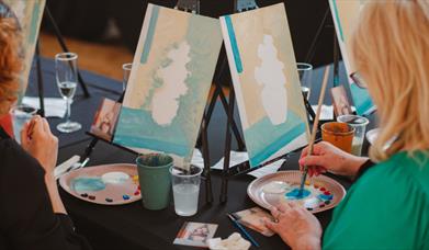 Image of a paint & prosecco session at the Ulster Museum showing two women painting canvases. 
