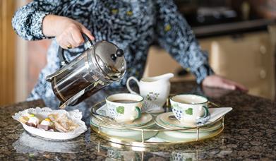 Image with owner pouring tea into cups with buns on a plate