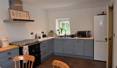 A kitchen with an antique style cooker, sink, microwave and fridge with a window.