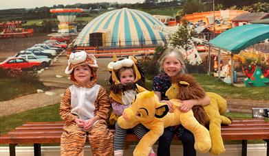 Three smiling children sitting on a bench, with two in animal costumes.