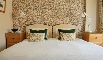 Image of a bed with patterned wall paper and matching cushions.