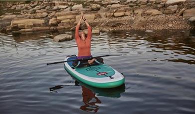 A person sitting in a yoga pose on a SUP board on water