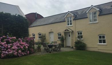 Image shows front of property with garden table and chairs on gravel drive. Also, lawn and rose bushes