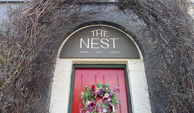 Archway over red door with sign reading The Nest and garland on the door