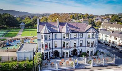 Beautiful exterior of Whistledown Hotel with blue skies, play park to the left and Warrenpoint Band Stand in the distance.