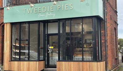 Exterior of Tweedie Pies Home Bakery with black framed glass, mint green sign and wooden panel trim