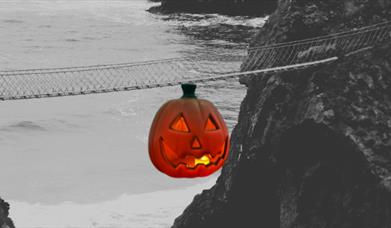 Black and White Picture of Carrick-a-Rede Rope Bridge  for Halloween, with a pumpkin graphic hanging from the bridge