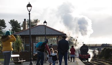 Steam train departing from Whitehead Station with family onlooking from platform