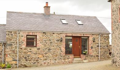 Image shows front of stone cottage with wooden door and gravel driveway.