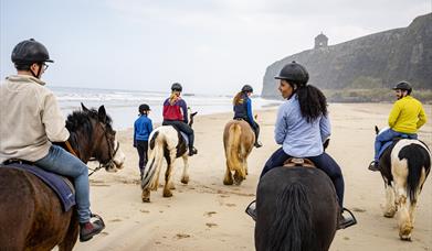 a group of people on horseback on Downhill Beach with Mussenden Temple visible in the distance