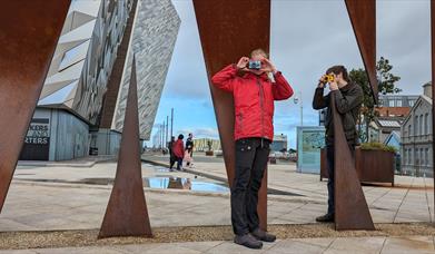 Two visitors taking pictures with Konica Pop cameras at the Titanic sign.