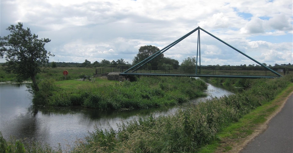 The Bann Weir in Portadown, Northern Ireland, with water cascading over the structure and lush green banks on either side.