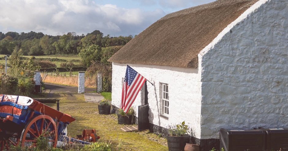 Arthur Cottage in Ballymena, a traditional thatched cottage with a white exterior and a small garden, under a blue sky.