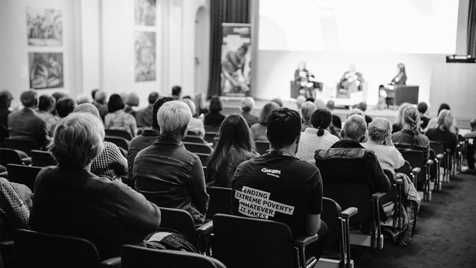 audience watching a discussion panel of 3 people on stage