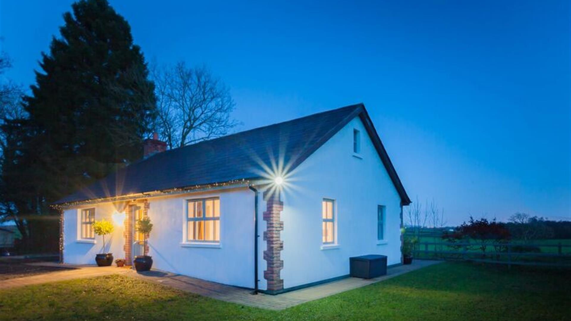 A cottage at night beside a country feild in front of a large tree.