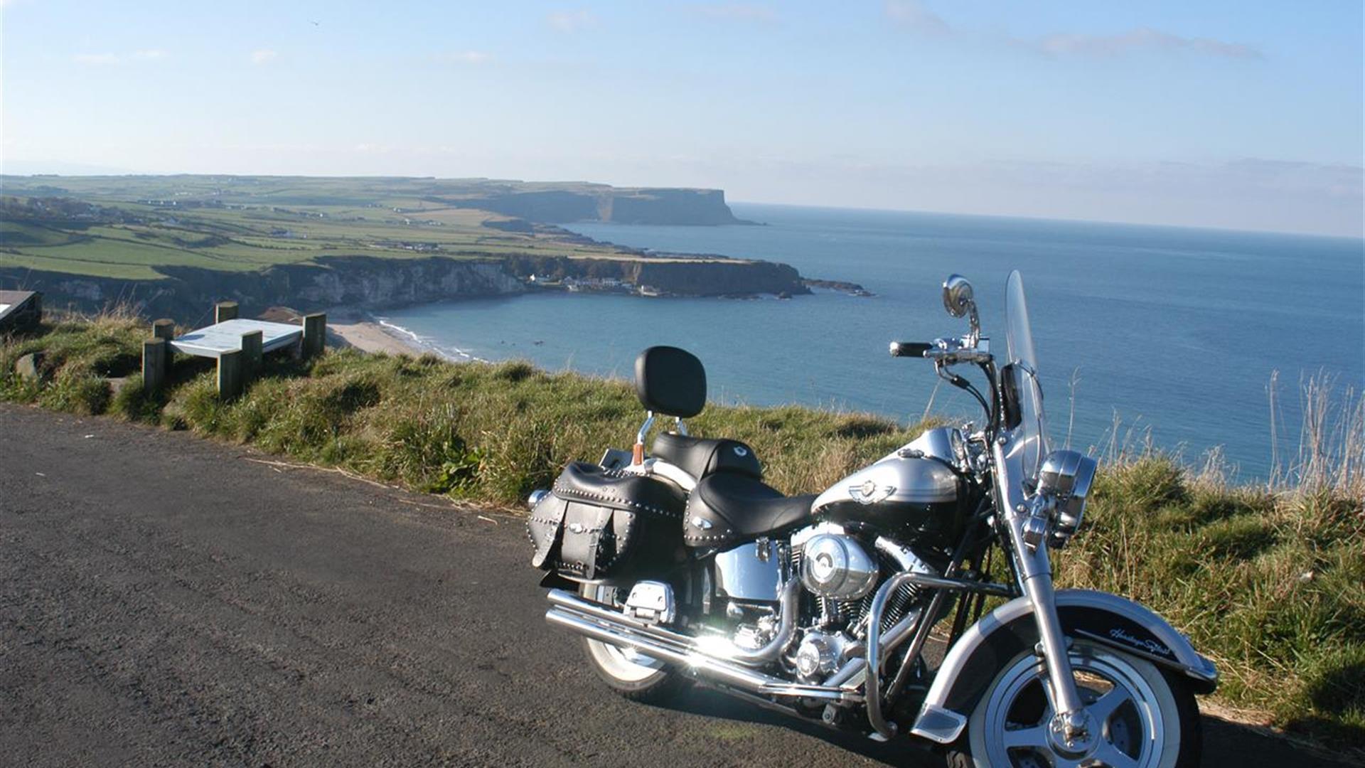 A Harley-Davidson on a road overlooking cliffs with a beach.