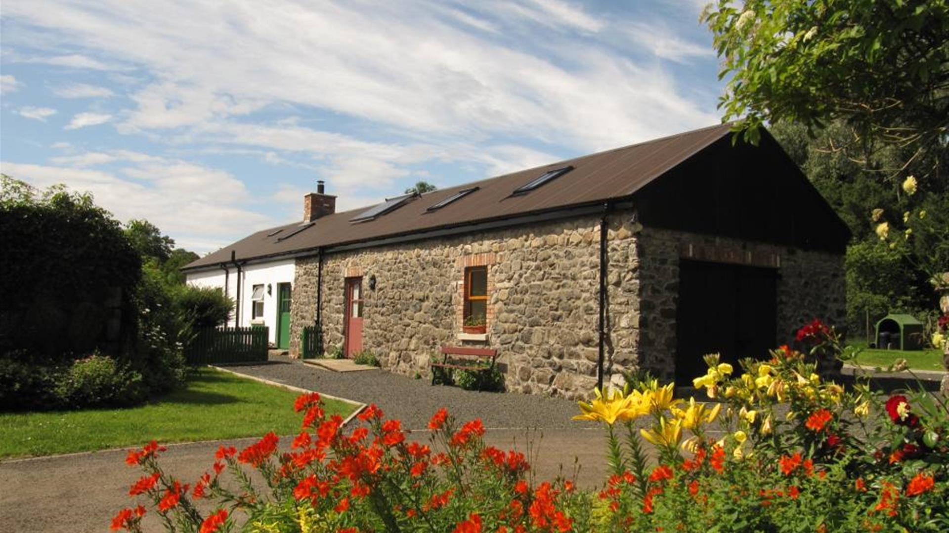 Converted cobblestone barn in the country with red and yellow flowers.