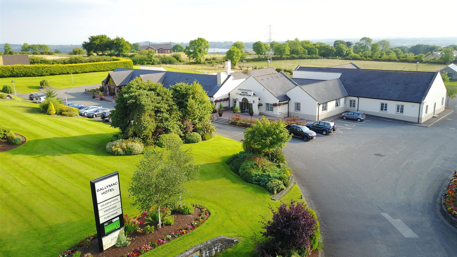 Image shows hotel and grounds with grass area and sign re hotel name. Also shows parking areas