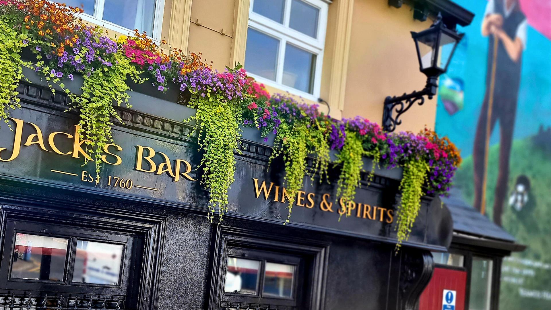 Exterior of Jack's Bar at Walsh's Hotel in Maghera, featuring a black facade with gold lettering that reads "Jack's Bar Wines & Spirits Est. 1760." Co