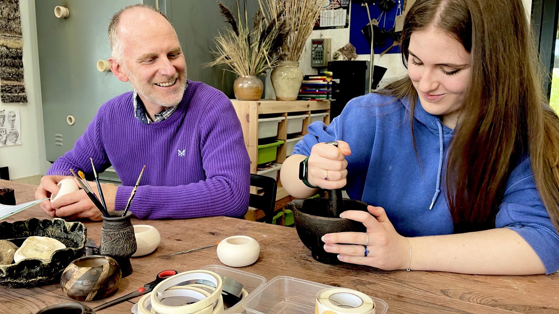 people sat at a table create designs on ceramic pots