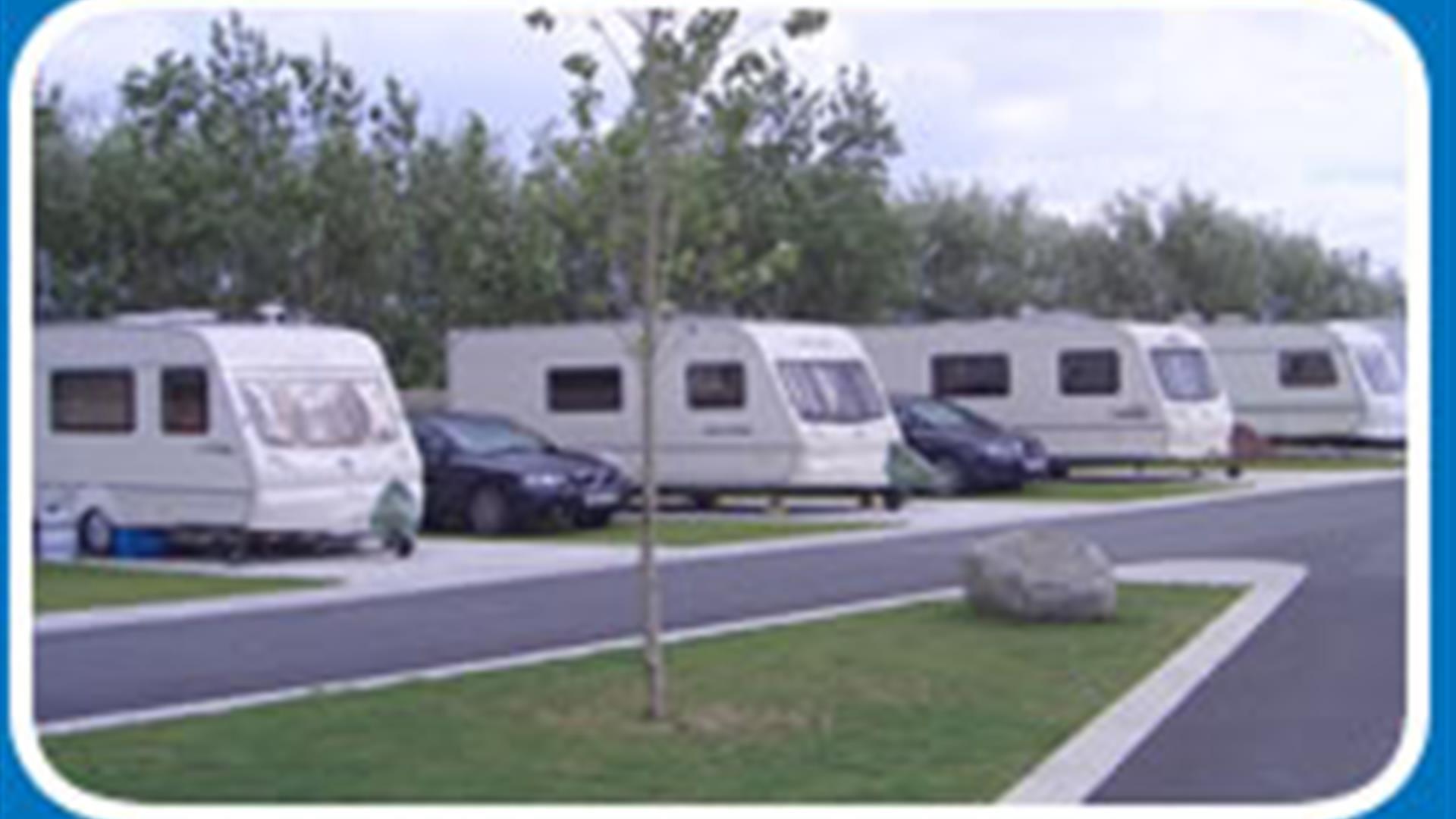 A road in a caravan park with 4 caravans and parked cars.