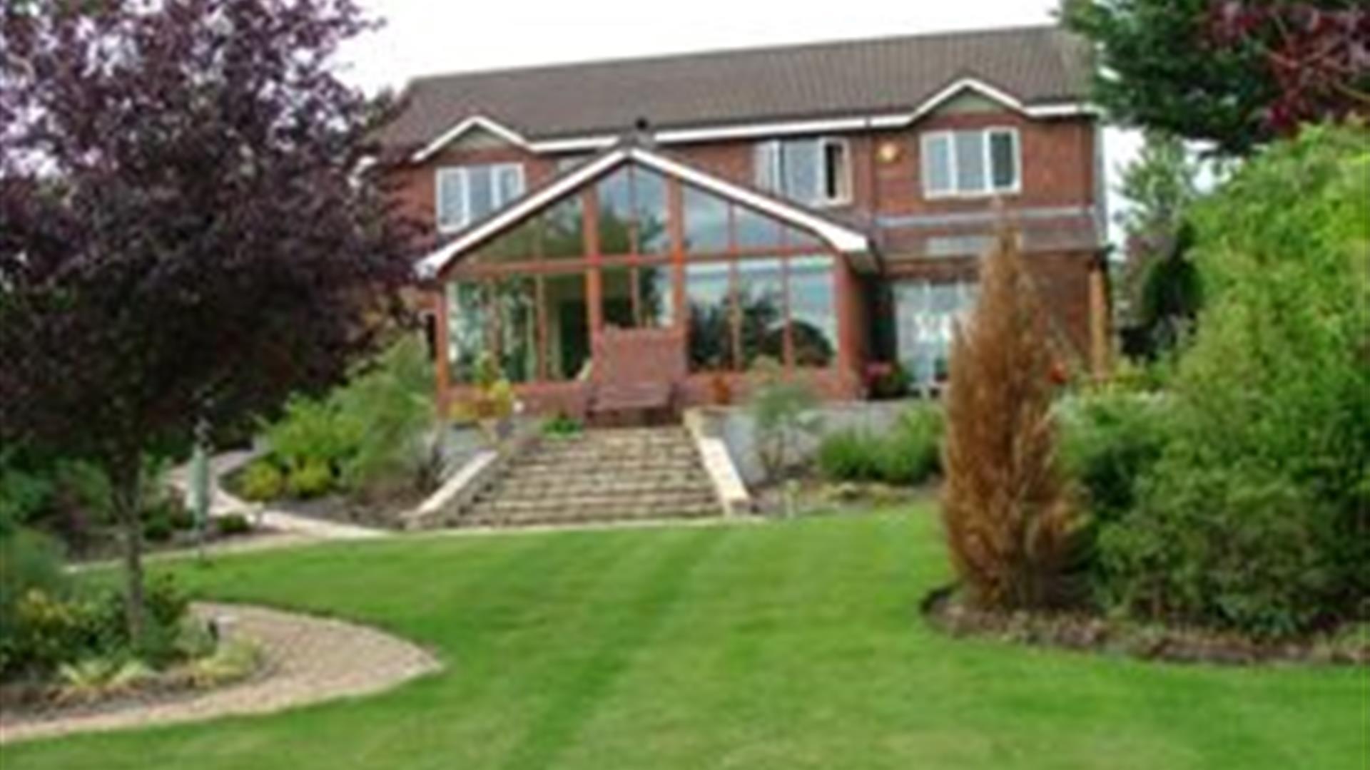 A large B&B on a lawn with trees and stone stairs leading to a large conservatory.