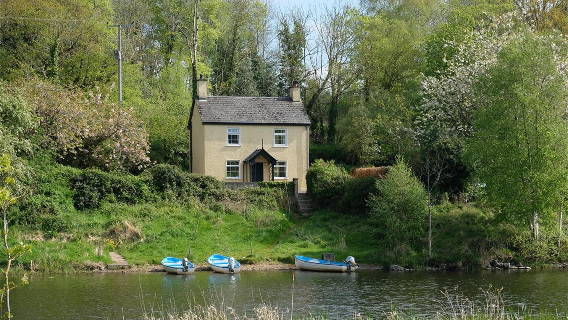 A house in a wooded area with a river and boats outside.