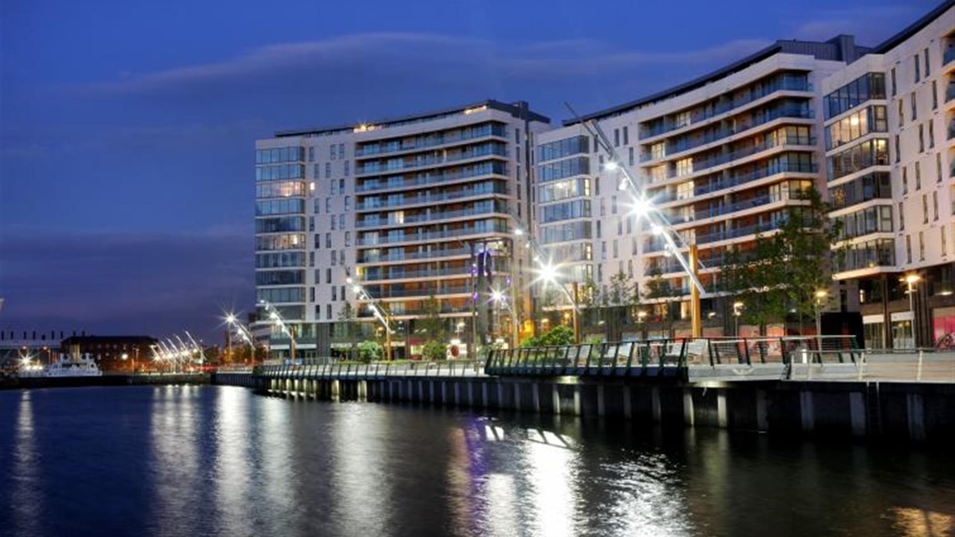 A curving apartment building at night on a seaside walkway.