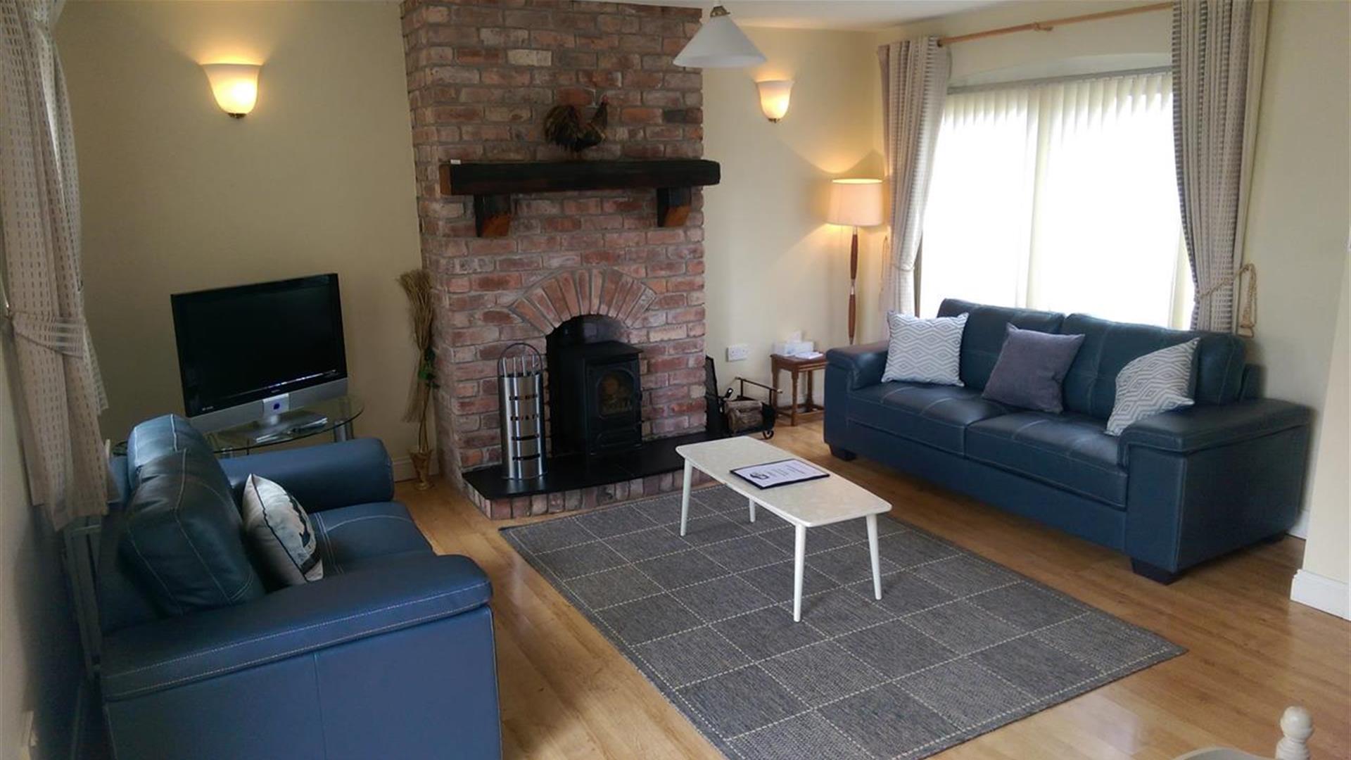 Image shows lounge area with 2 sofas, fireplace and wooden floor