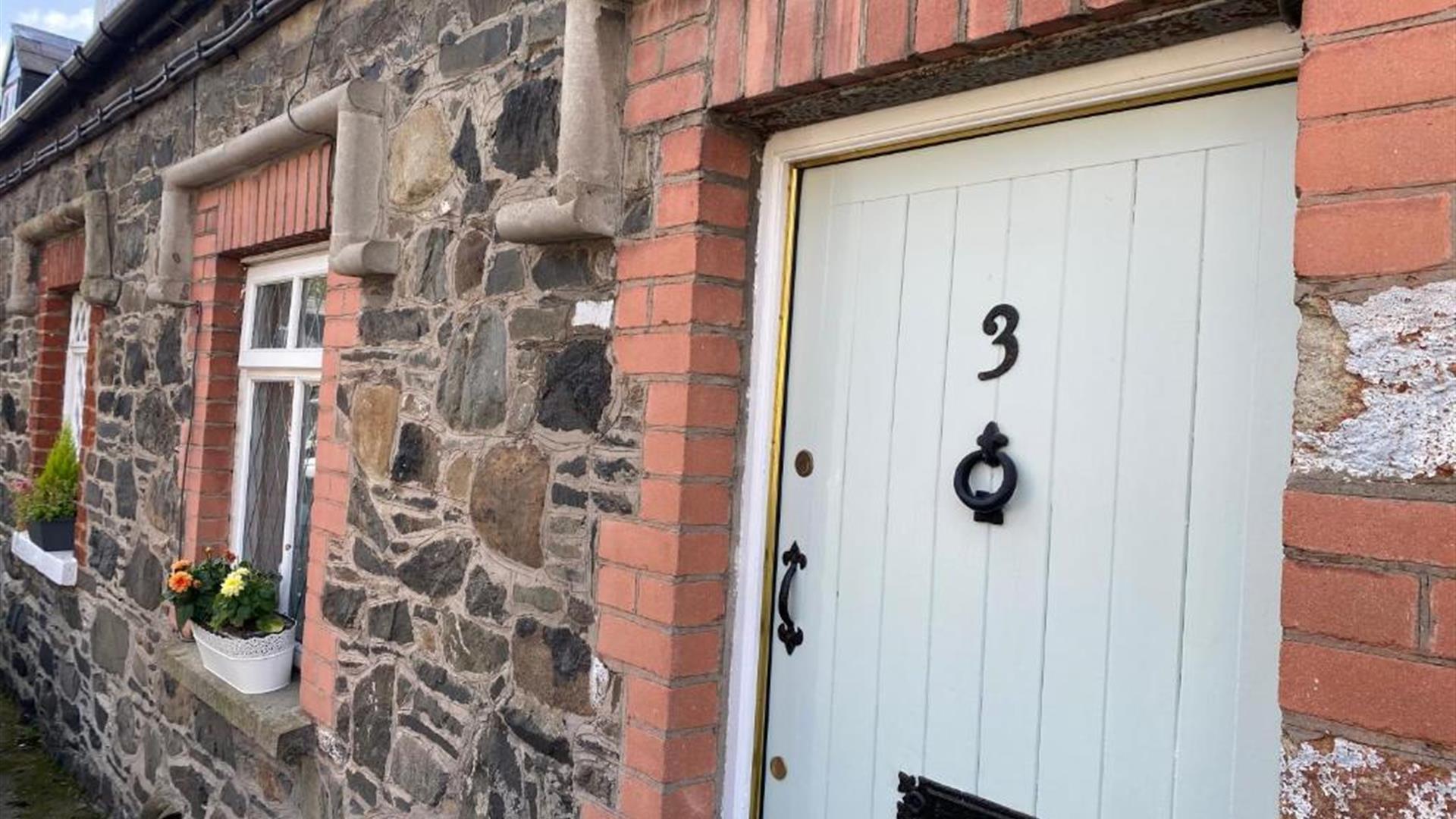 Image shows front door of property with flower beds on window sills