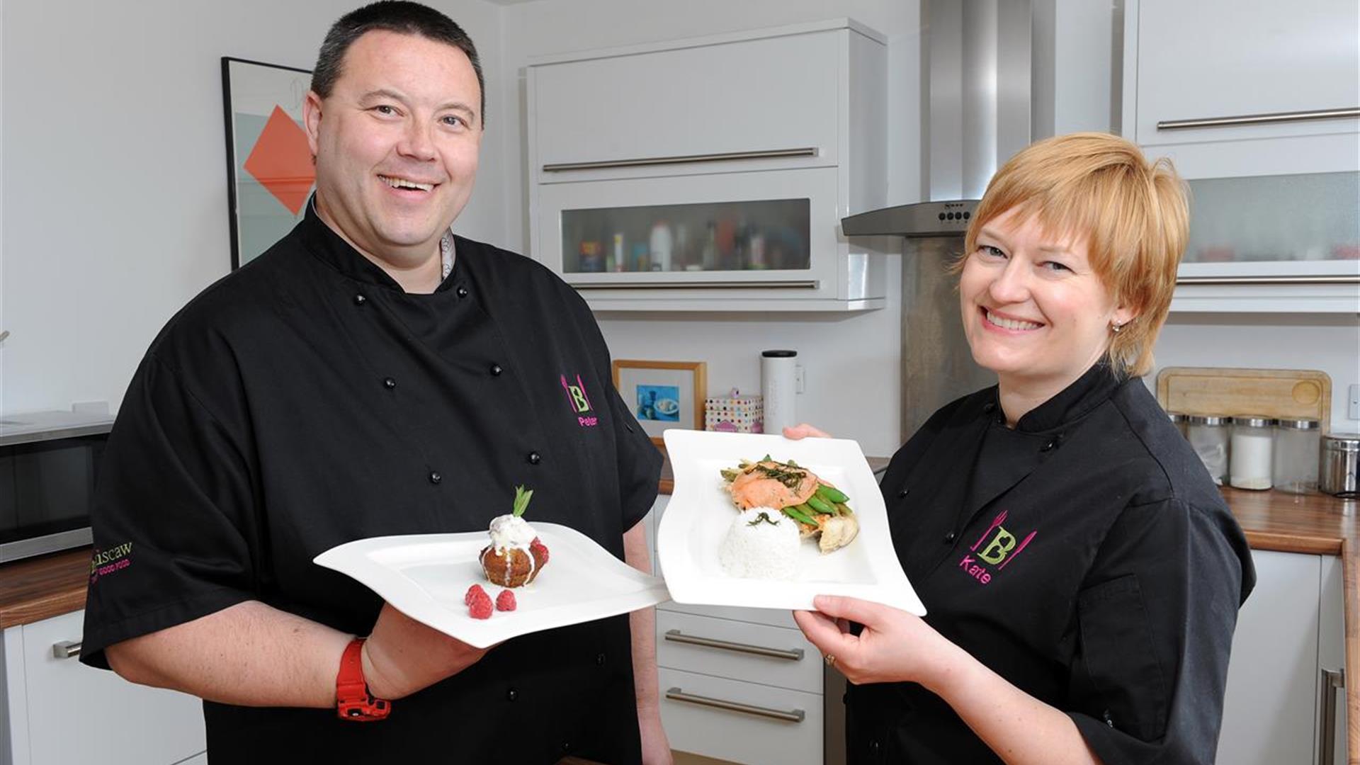 Two teacher chefs smiling and holding plates of food.